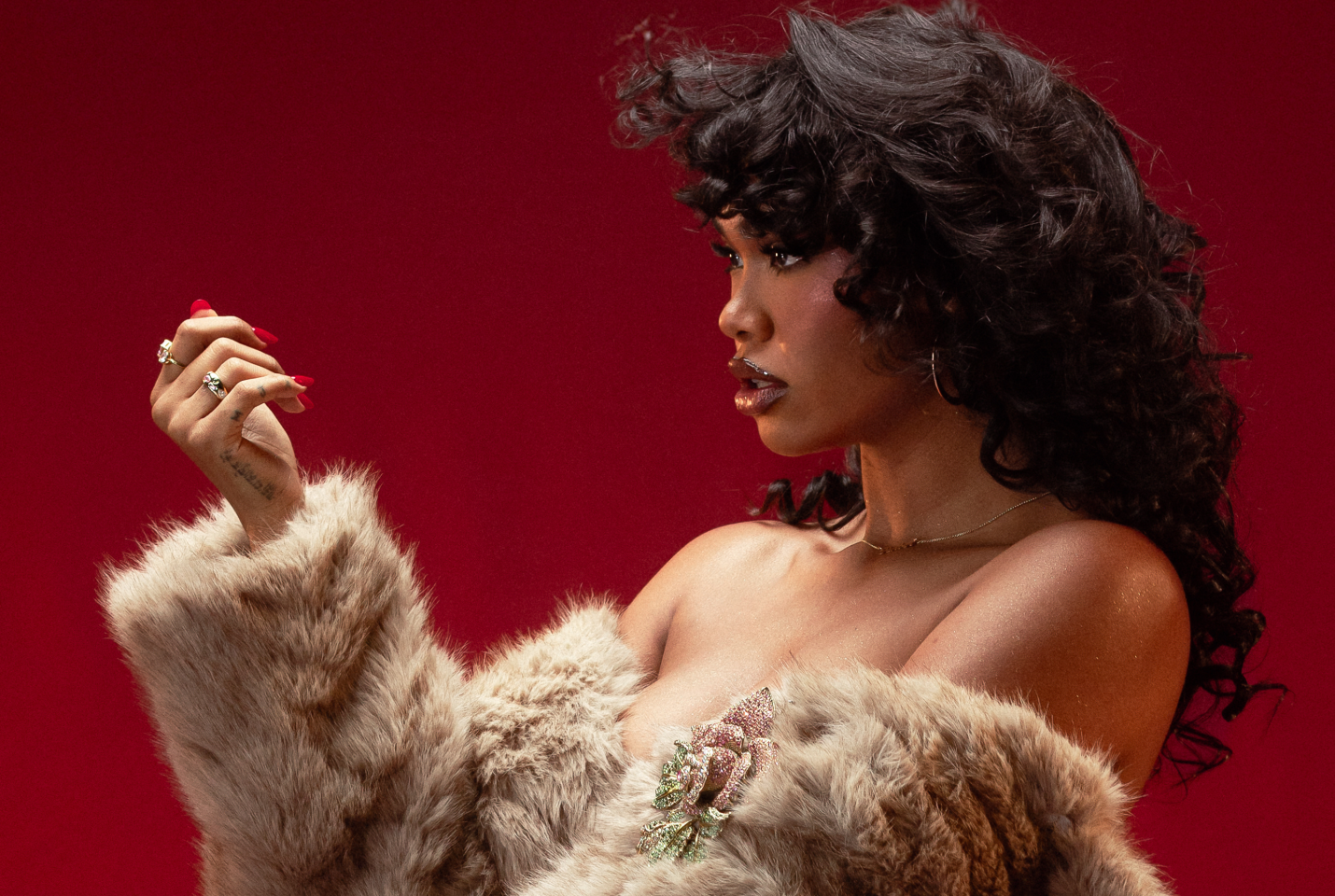 Musician Amber Mark facing right looking at her hand in front of red backdrop.